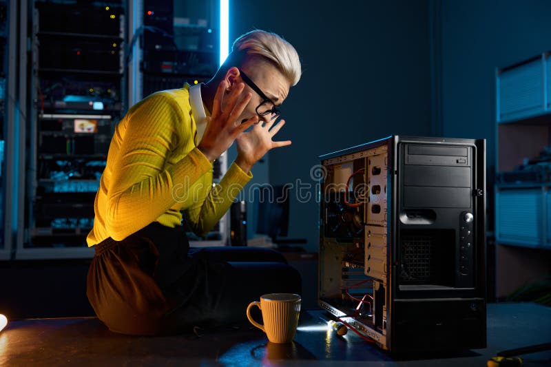 Joven mujer técnica de tecnología de la información gritando loca mirando la parte de la computadora rota. Una joven técnica de tecnología de la información gritando loca mirando la parte de la computadora rota mientras trabaja en la sala de servidores del centro de datos por la noche