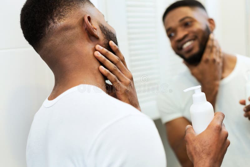 Joven negro aplicando hidratante en la barba en el baño