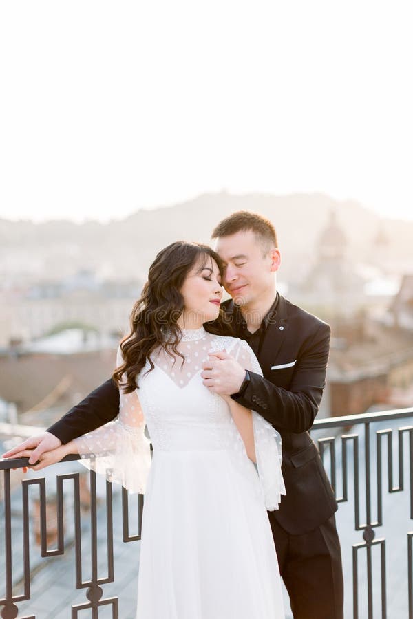 Joven novia y novio asiático, pareja feliz al atardecer en la vieja ciudad europea. La historia del amor de boda en Europa fotografía de archivo libre de regalías Joven novia y novio asiático, pareja feliz al atardecer en la vieja ciudad europea. La historia del amor de boda en Europa fotografía de archivo libre de regalías