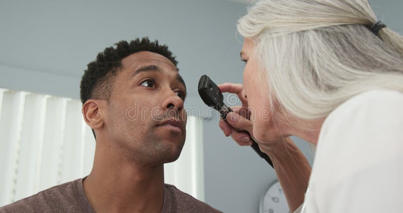 Joven paciente masculino negro con los ojos revisados por una doctora mayor