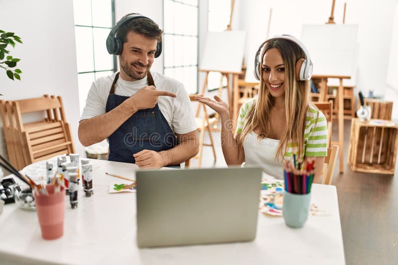 Joven pareja de esposa y marido en el estudio de arte mirando el video en el portátil sorprendido y sonriendo a la cámara mientras imagenes de archivo