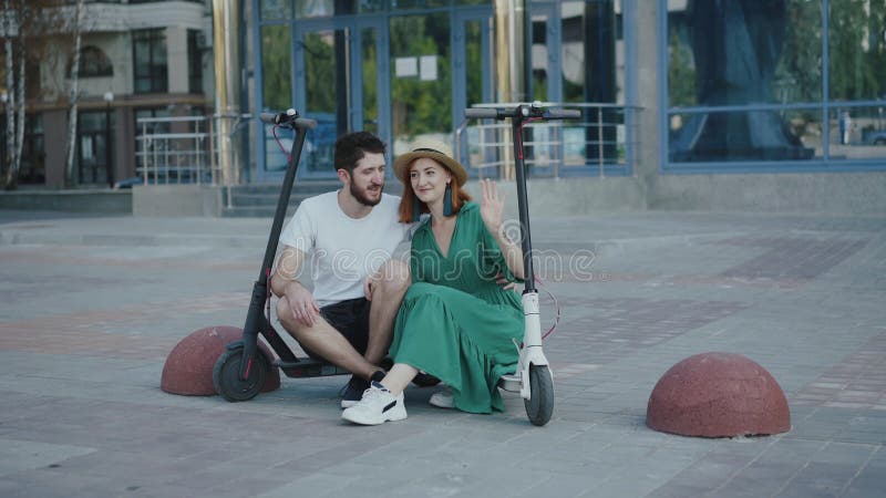 Joven pareja encantadora relajarse entre scooters eléctricos y divertirse