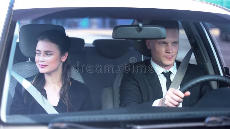 Joven pareja sonriendo modesto en primera cita, sentada en el coche, romance