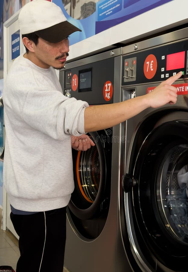 Joven poniendo ropa para lavar en una lavandería imagen de archivo libre de regalías