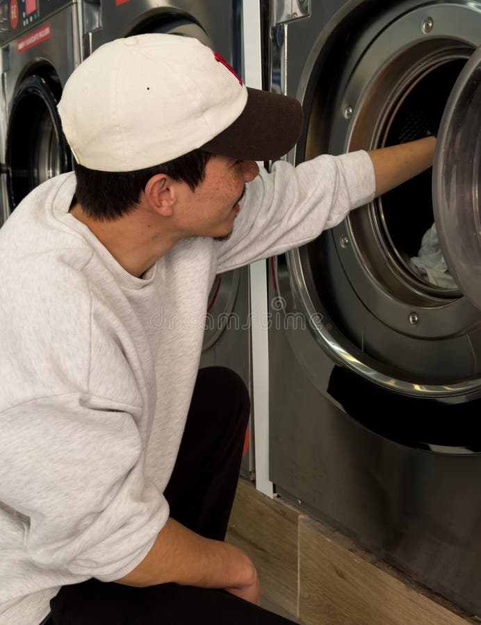 Joven poniendo su ropa en la lavadora en una lavandería automática imagen de archivo