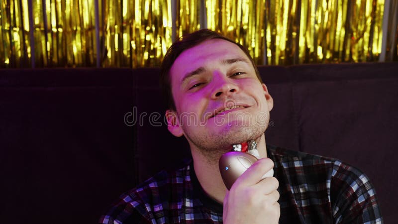 Joven sonriendo mirando la cámara y usando un masajeador 3d para la cara. relajación de los hombres sentados en el sofá y usando e