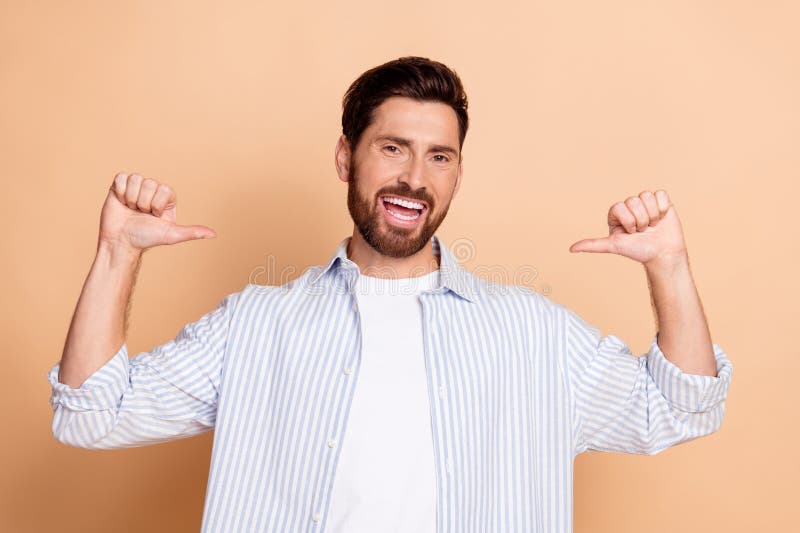 Joven sonriente con barba usando camisa a rayas haciendo gesto de mano segura contra fondo beige imagen de archivo libre de regalías