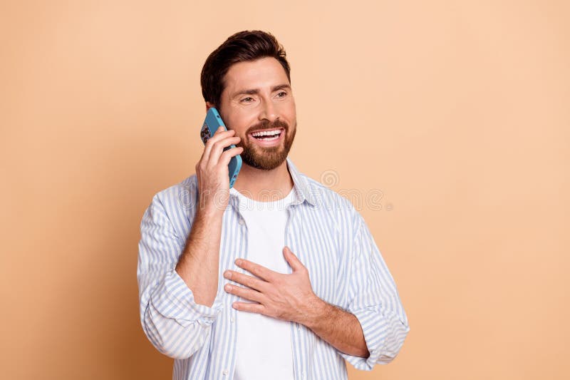 Joven sonriente mostrando una expresión alegre mientras realizaba una llamada telefónica en un entorno beige fotografía de archivo