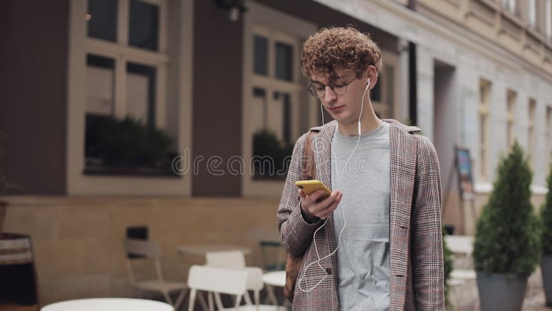 Joven tipo de pelo de rizo rojo hipster en lentes con auriculares con chaqueta chaqueta chaqueta chantajeada con amigos, usando s