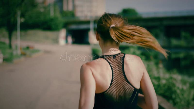 Joven trotando cerca del río en la ciudad. Vista posterior del trompo femenino almacen de video