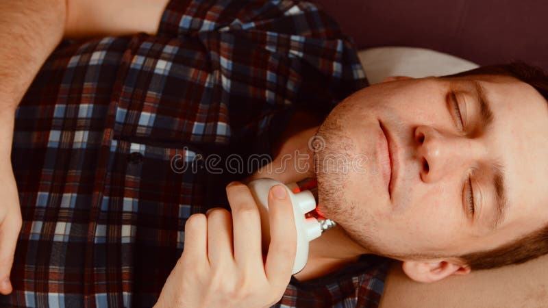 Joven usando un masajeador 3d para la cara. macho relajado con los ojos cerrados en el sofá y con el masaje eléctrico. concepto