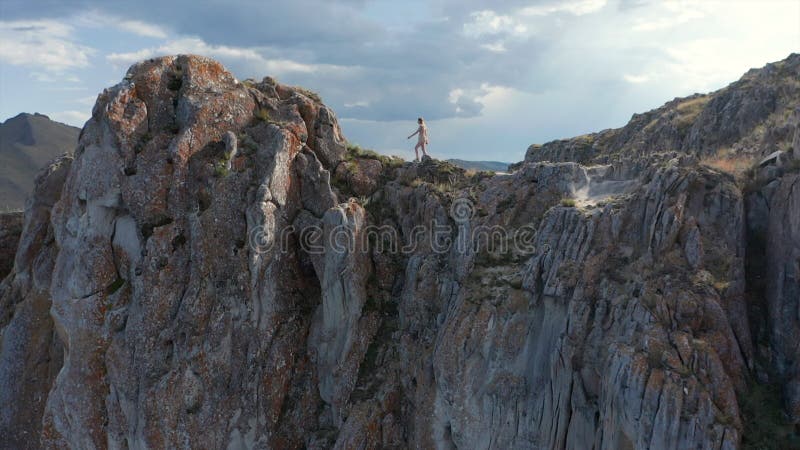 Joven vestida de blanco corriendo sobre la montaña por encima de los acantilados del lago