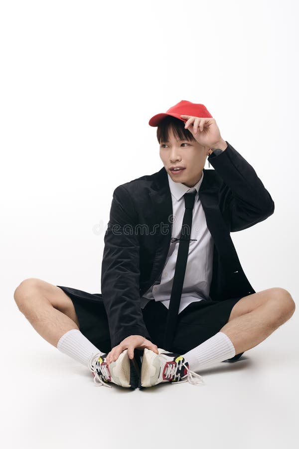 Joven y guapo hombre asiático posa con estilo. Joven encantador exhibe moda moderna con confianza sentada cómodamente en un estudio.