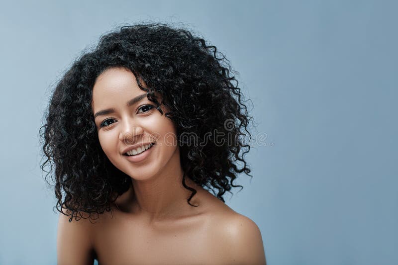 Joven y hermosa hembra con pelo rizado negro mirando la cámara imagen de archivo