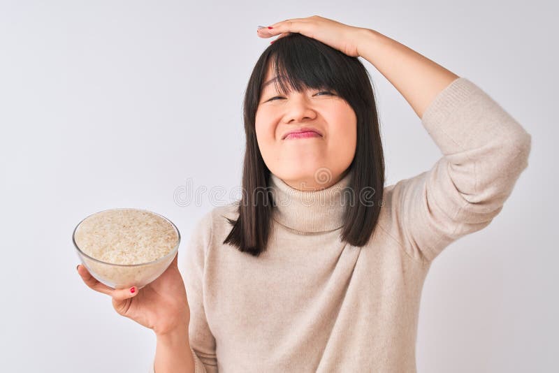 Joven y hermosa mujer china sosteniendo el tazón con arroz sobre fondo blanco aislado estresada con la mano en la cabeza impactada imágenes de archivo libres de regalías