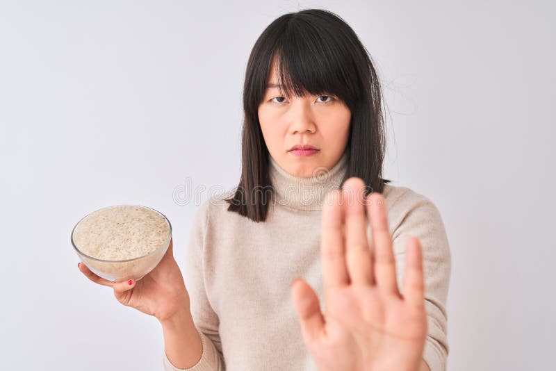 Joven y hermosa mujer china sosteniendo el tazón con arroz sobre fondo blanco aislado con la mano abierta haciendo signo de detene fotografía de archivo libre de regalías