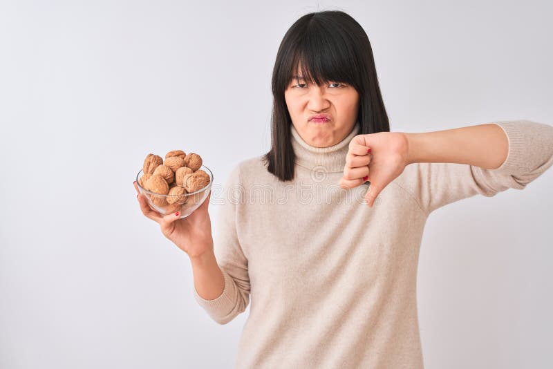 Joven y hermosa mujer china sosteniendo un bol con nueces sobre fondo blanco aislado con cara enojada negativa mostrando imagen de archivo libre de regalías