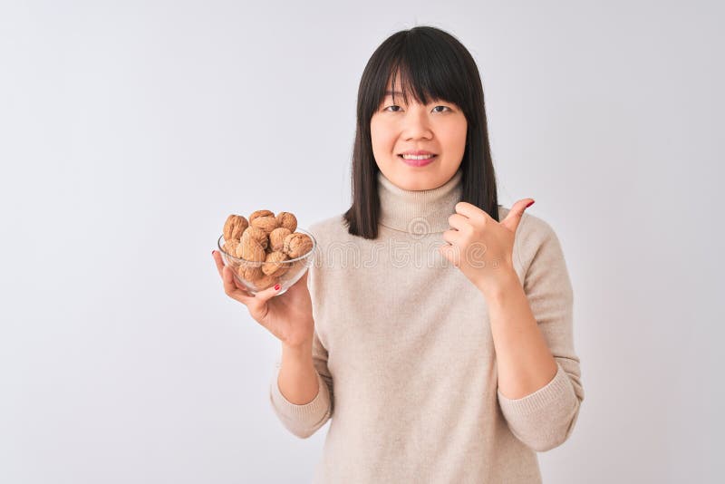 Joven y hermosa mujer china sosteniendo un tazón con nueces sobre fondo blanco aislado feliz con una gran sonrisa haciendo bien el fotografía de archivo
