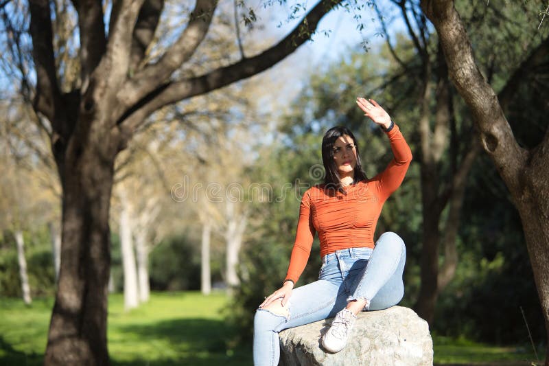 Joven y hermosa mujer con camiseta naranja y jeans cubriéndose la cara de los rayos de sol con la palma de la mano relajada y fotos de archivo libres de regalías