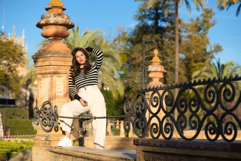 Joven y hermosa mujer con el largo pelo castaño vestido con una camiseta de rayas negras y blancas y pantalones blancos descansa e fotos de archivo