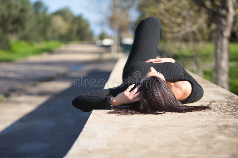 Joven y hermosa mujer con traje de salto negro relajada y tranquila tendida sobre una pared de piedra. moda de belleza relajación foto de archivo libre de regalías