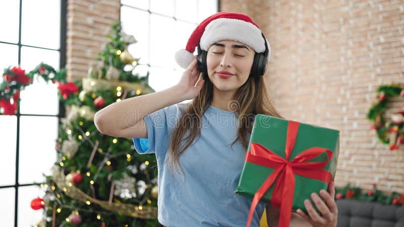 Joven y hermosa mujer hispana escuchando música sosteniendo regalos celebrando navidades en casa foto de archivo libre de regalías
