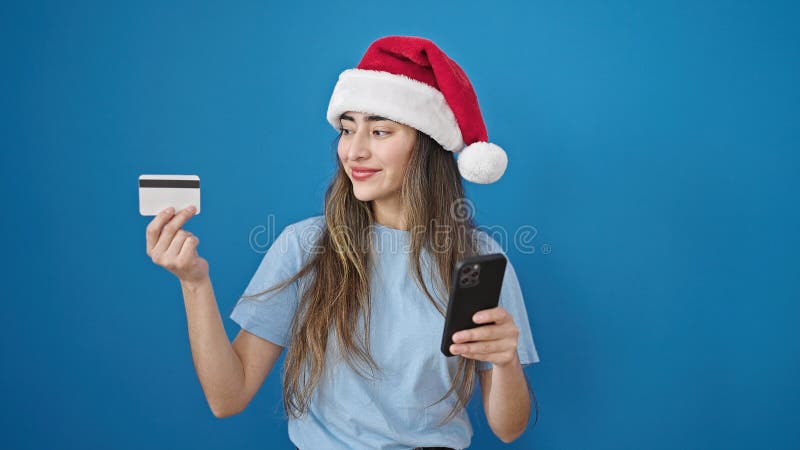 Joven y hermosa mujer hispana haciendo navidad en línea comprando con smartphone sobre fondo azul aislado foto de archivo libre de regalías