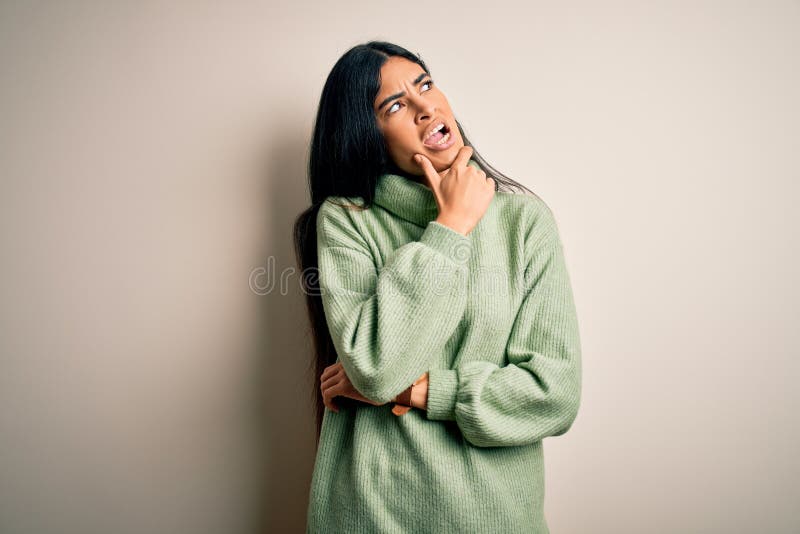 Joven y hermosa mujer hispana que usa suéter verde de invierno sobre un fondo aislado pensando preocupados por una pregunta preocu. Joven y hermosa mujer hispana que usa suéter verde de invierno sobre un fondo aislado pensando en una pregunta preocupada y nerviosa con la mano en la barbilla