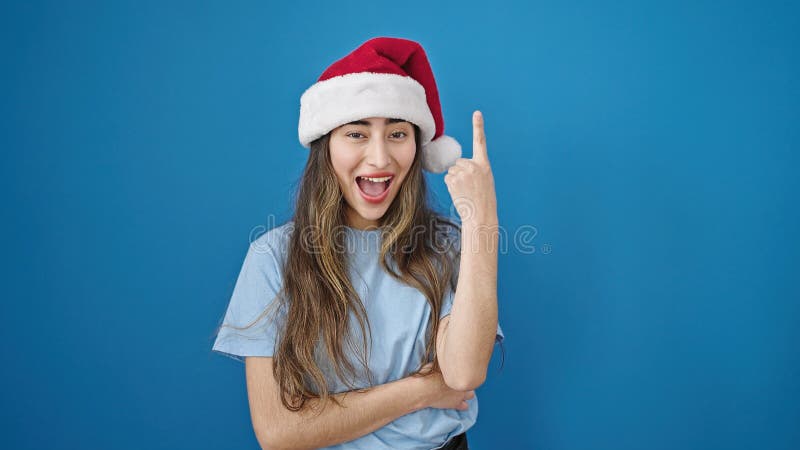 Joven y hermosa mujer hispana sonriendo con sombrero de navidad que tiene una idea sobre un aislado fondo azul imagen de archivo