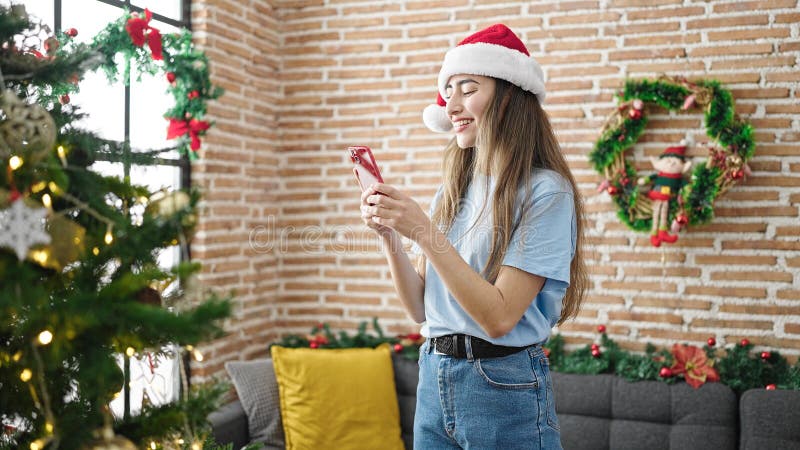 Joven y hermosa mujer hispana usando un smartphone celebrando navidades en casa fotos de archivo