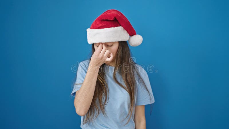 Joven y hermosa mujer hispánica con sombrero de navidad con dolor de cabeza sobre fondo azul aislado imagen de archivo