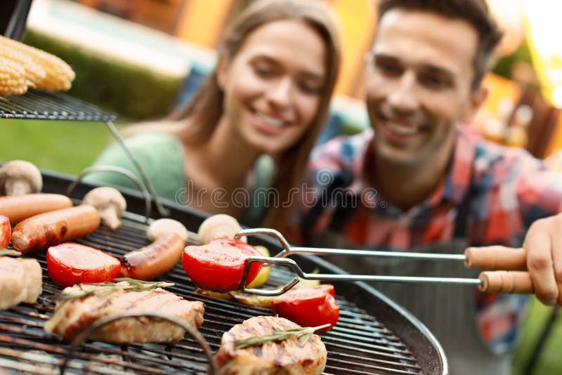Joven y mujer cerca de parrillada asada, se concentra en las tonalidades con tomate imagen de archivo libre de regalías Joven y mujer cerca de parrillada asada, se concentra en las tonalidades con tomate imagen de archivo libre de regalías
