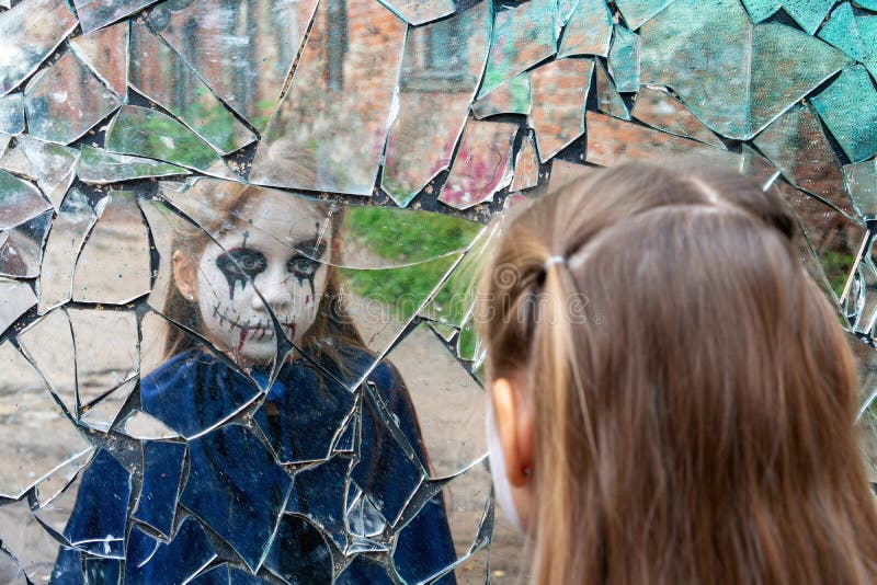 Young girl zombie looks in a broken mirror. The concept of human emotions. Young girl zombie looks in a broken mirror. The concept of human emotions.