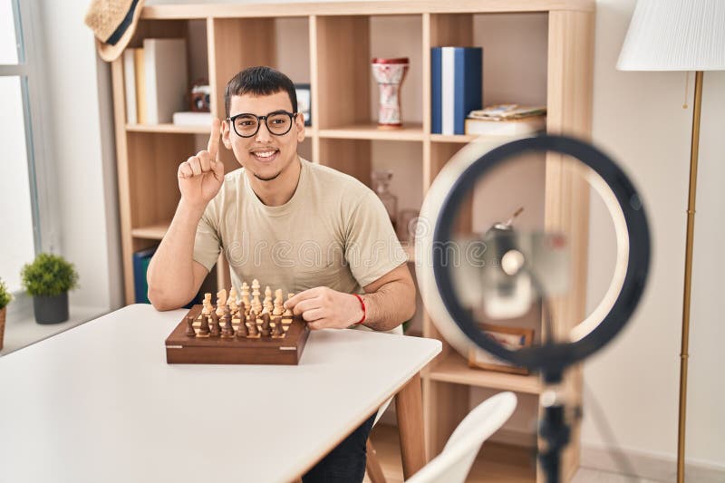 Joven árabe haciendo tutorial de ajedrez sonriendo con una idea o una pregunta señalando con el rostro feliz número uno imagen de archivo libre de regalías