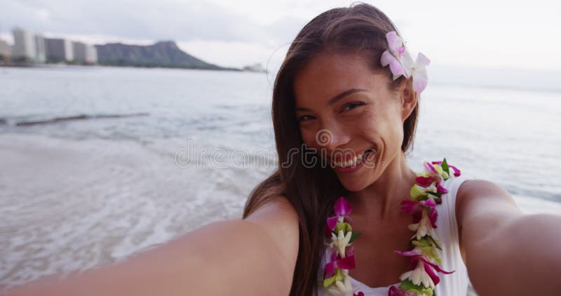 Jovencita alegre de lei garland tomando selfie en la playa de waikiki