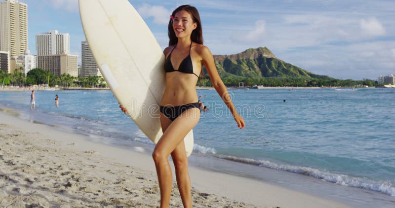 Jovencita alegre que lleva tablas de surf mientras corre en la playa de waikiki