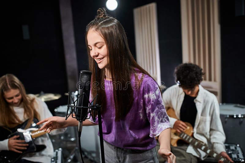 cheerful brunette teenage girl singing happily with her friends playing instruments in studio, stock photo. cheerful brunette teenage girl singing happily with her friends playing instruments in studio, stock photo