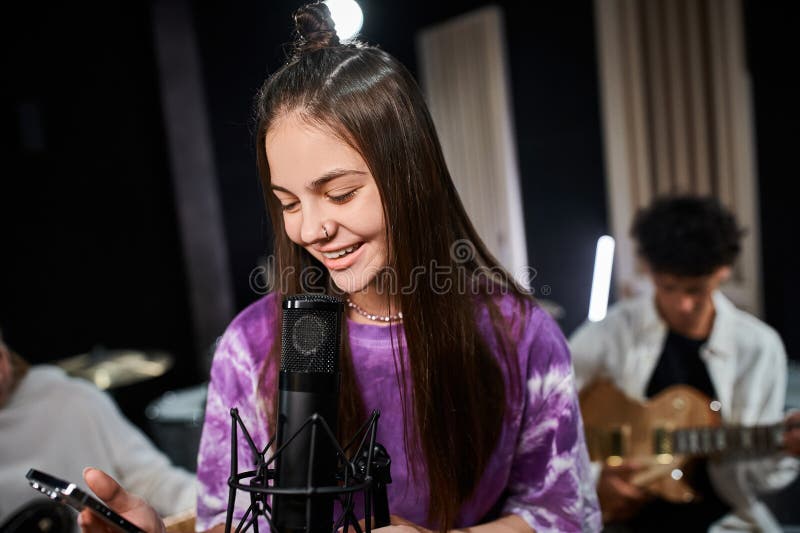 jolly cute teenage girl with piercing singing and looking at mobile phone next to her friends, stock photo. jolly cute teenage girl with piercing singing and looking at mobile phone next to her friends, stock photo