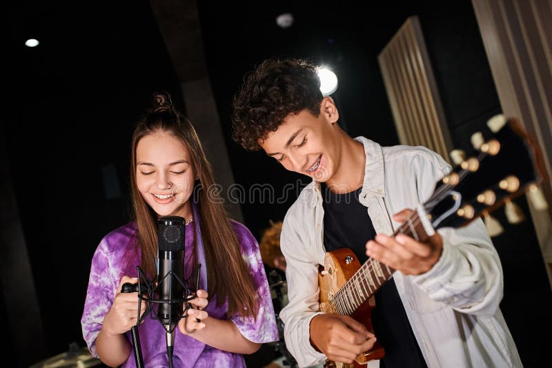 cheerful cute teenage girl in vibrant attire singing into microphone next to her guitarist, stock photo. cheerful cute teenage girl in vibrant attire singing into microphone next to her guitarist, stock photo