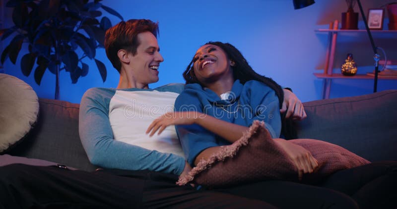 Jovencita pareja alegre pasándola bien sentada en el sofá frente a la televisión. feliz chico milenario y su novia metrajes
