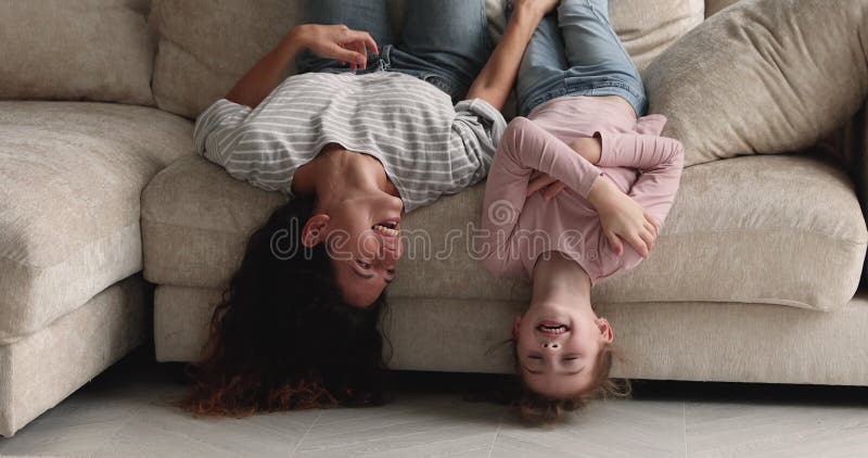 Jovencita y alegre madre y niño boca abajo en el sofá.