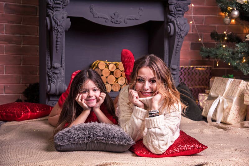 Jovencita y bonita madre con hija tendida cerca del árbol de navidad frente a la chimenea concepto de navidad de año 2022 fotografía de archivo