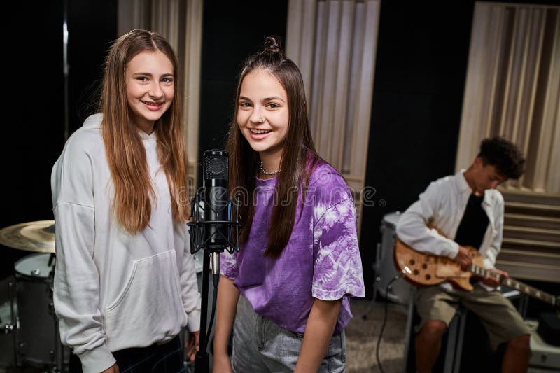 joyful pretty teenage girls looking at camera near microphone with their friend playing guitar, stock photo. joyful pretty teenage girls looking at camera near microphone with their friend playing guitar, stock photo