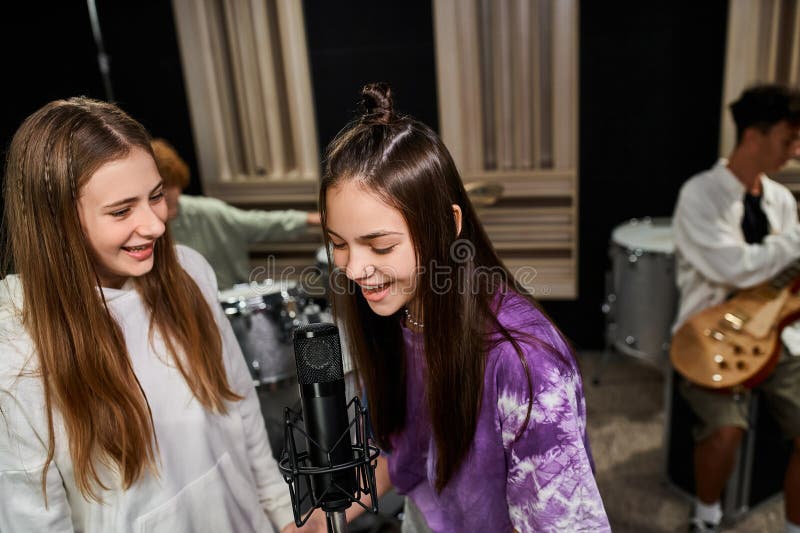 cheerful adorable teenage girls singing into microphone and boy playing instruments in studio, stock photo. cheerful adorable teenage girls singing into microphone and boy playing instruments in studio, stock photo