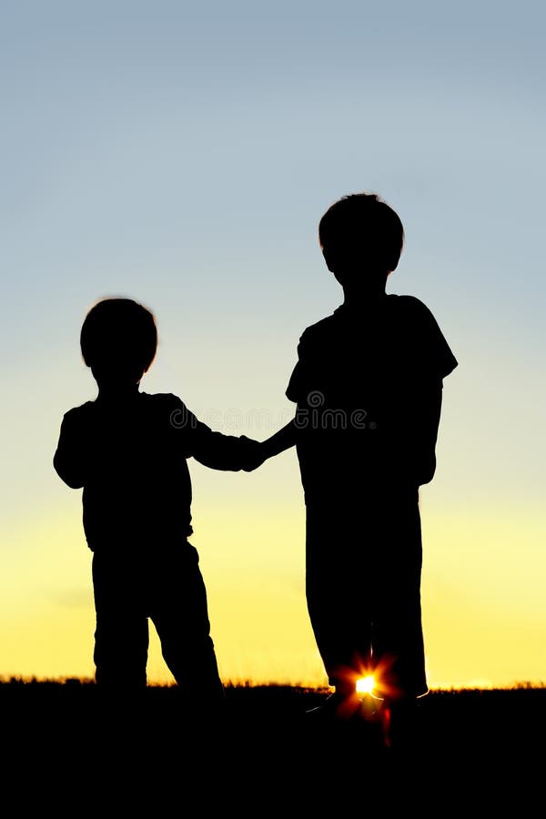Jovens crianças da silhueta que guardam as mãos no por do sol imagens de stock royalty free Jovens crianças da silhueta que guardam as mãos no por do sol imagens de stock royalty free
