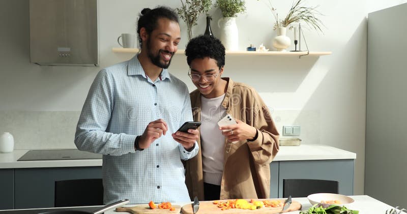 Jovens esposas negros conversam sobre smartphones na cozinha