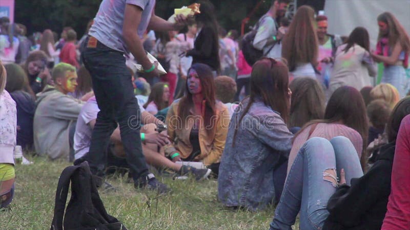 Jovens felizes no festival do ar livre que senta-se na grama que come os petiscos, conversando