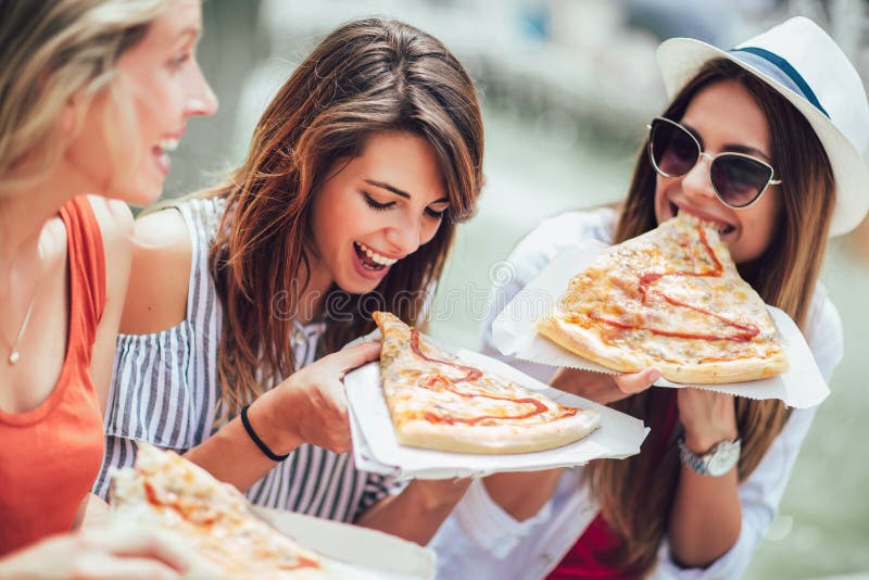 Jovens mulheres bonitas que comem a pizza após a compra, tendo o divertimento junto