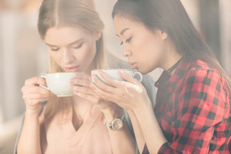 Jovens mulheres bonitas que guardam os copos brancos e que bebem o café fresco do café fotografia de stock Jovens mulheres bonitas que guardam os copos brancos e que bebem o café fresco do café fotografia de stock
