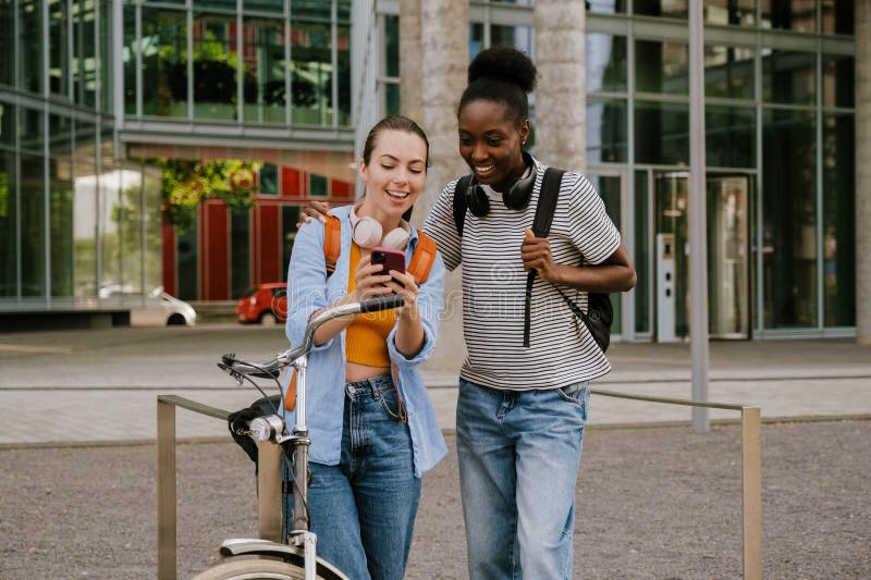 Jovens mulheres multirraciais sorrindo e usando celular na rua da cidade fotos de stock
